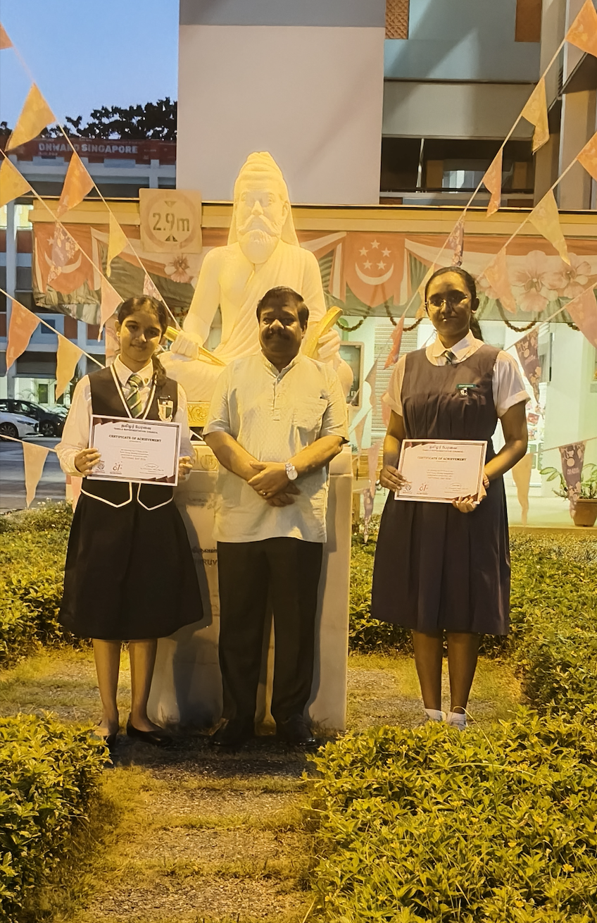 2 female students standing on either side of a male teacher, with certificates in their hands, smiling at the camera.
